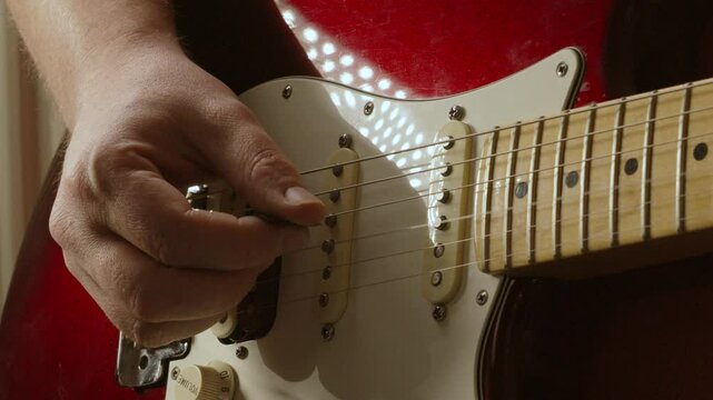 Guitarist Gently Plucking Strings with Plectrum on Red Stratocaster Guitar in Slow Motion in Natural Lighting Environment 4K