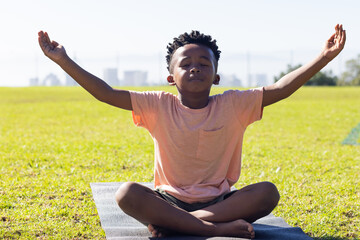 Meditating on yoga mat, african american boy practicing mindfulness outdoors in school setting