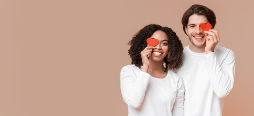 True Love. Portrait of happy interracial couple with red paper hearts over eyes posing together...