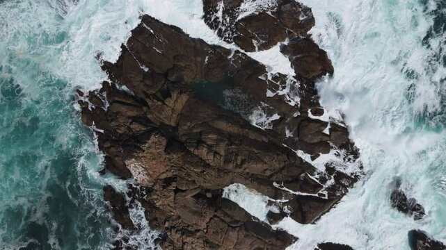 Aerial birds eye view showcases the rugged rocky outcrop surrounded by crashing waves at Playa Chica, located in Quintay, Casablanca, Valpara&iacute;so, Chile. Rising Shot