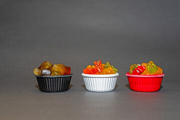 Colourful and small gel candies in small bowls. Grey ground and background.