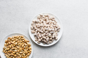 Overhead view of raw coated peanuts on a white plate, flatlay of peanuts coated in egg and flour on a marble countertop, top view of nigerian peanut snack