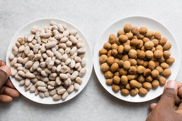Overhead view of raw coated peanuts and fried coated peanuts on a white plate, flatlay of coated peanuts on a marble countertop, process of making coated nuts or cracker nuts