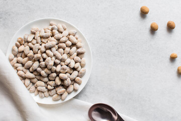 Overhead view of raw coated peanuts on a white plate, flatlay of peanuts coated in egg and flour on a marble countertop, top view of nigerian peanut snack