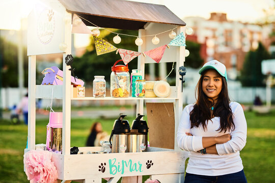 Girl, portrait and cake stall outdoor for hospitality industry, dessert sale or confectionary of small business. Smile, woman and arms crossed with food cart, bakery choice and selling snack at park
