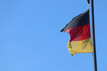 German flag flying on the wind. Waving flag of Germany on flagpole against blue sky. Deutschland. Black, red and yellow colors on German flag in a front of Bundestag. Symbol of German people. 