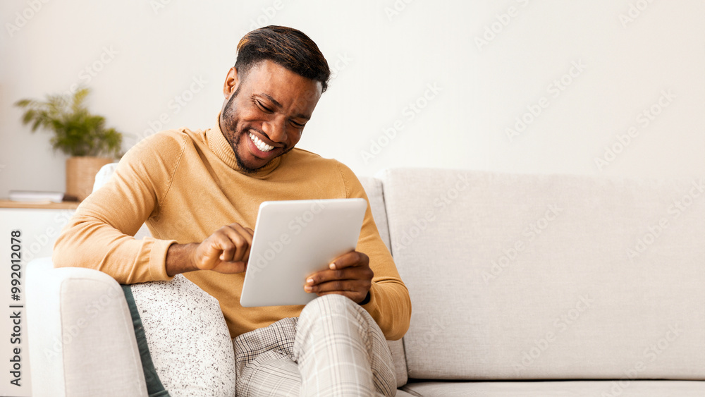 Poster cheerful black guy using digital tablet smiling sitting on sofa at home. cool mobile application. se
