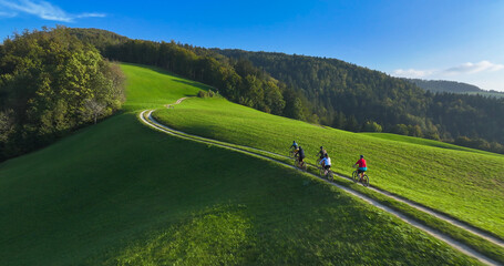AERIAL: Cycling friends enjoying a serene ride along a green hilltop bike trail bathed in gentle...