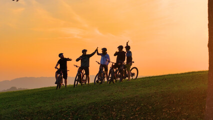SILHOUETTE: Golden sunset and a group of mountain bikers celebrating on top of the hill after...