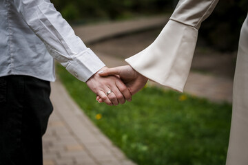 Romantic Close-Up of Intertwined Hands of Bride and Groom on a Serene Pathway