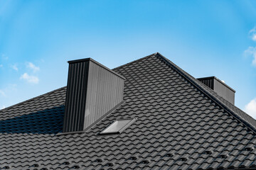 The rooftop features a sleek black tile design, highlighted by dual chimneys and a skylight, all set against a vibrant blue sky on a sunny day