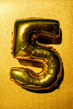 Green number 5 balloon on a glittering gold background