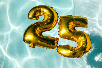 Golden 25th anniversary balloons floating in a pool