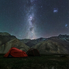 Starry Night Sky and Milky Way Above Mountain Campsite.

A stunning capture of the Milky Way stretching across a clear night sky above a remote mountain campsite. Two illuminated tents add a human ele
