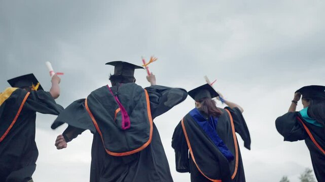 Four graduates are standing on a hill, holding their graduation caps and gowns. Scene is celebratory and proud, as the graduates are about to receive their diplomas