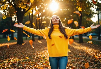 A young woman in a yellow sweater and blue jeans, surrounded by autumn leaves, is joyfully spreading them while smiling, with the sun casting a warm glow and the trees in the background