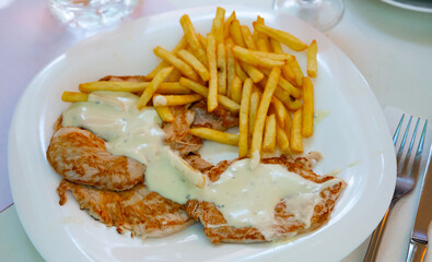 Delicate grilled pork tenderloins in cheese cream sauce with garnish of fried potatoes
