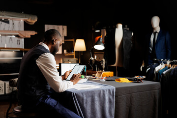 Skilled couturier meticulously reviewing collection of handdrawn sketches in order to conceptualize...