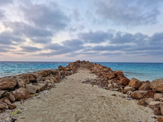 This breathtaking photograph captures the rugged beauty of a stone pathway stretching toward the vast horizon of the ocean.