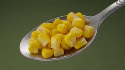 Silver spoon holding bright yellow sweet corn kernels against a green background. Close-up, shallow dof.