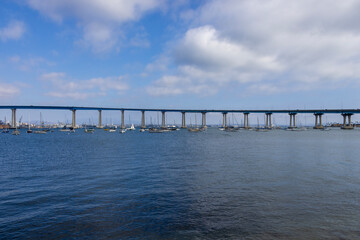 Obraz premium San Diego bay and the Coronado Bridge with ships sailing on blue ocean water, office buildings and skyscrapers along the coast at Coronado Tidelands Park in Coronado California