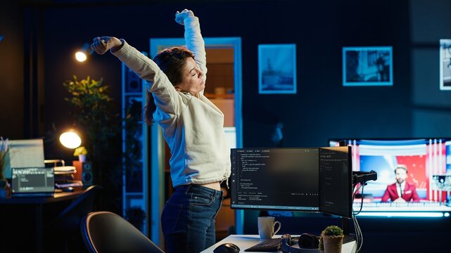 Programmer stretches body limbs after securing company servers from virus attacks all day. Fatigued IT remote employee relaxing tense muscles at desk after building firewalls protecting data, camera A