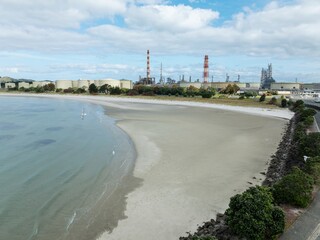 Fototapeta premium Chimney stacks, beach and storage tanks at the decommisioned Marsden Point Refinery, Whangarei, Northland, New Zealand.