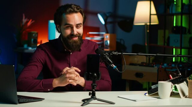 Media star talking in front on smartphone attached to tripod stabilizer in studio, discussing with viewers. Man using mobile phone to record video in living room for social media, camera A