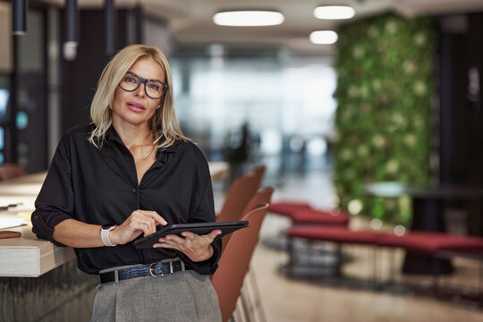 A Professional Woman in a Modern Office Environment is Holding a Tablet in Her Hands