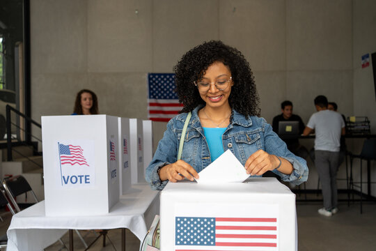 portrait of a young african american woman voting in the us election, placing vote ballot in the polling box, vote in America. Concept of usa choice, democracy and freedom