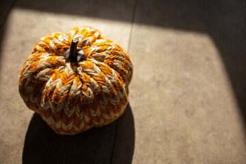 close-up of a striped white and orange pumpkin made of yarn in warm moody lighting 
