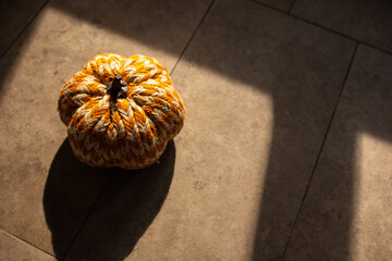 close-up of a striped white and orange pumpkin made of yarn in warm moody lighting 