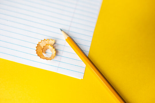 flat lay of a sharpened number two pencil, a pencil shaving, blank notebook paper against a bright yellow background