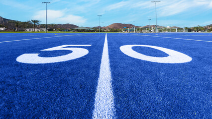 Looking down the 50 yard line on a blue turfAmerican football field
