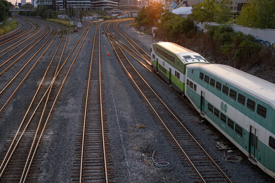 Aerial view of GO train passing by district with high rise tall buildings in the city center at sunrise hour. Commute, urban transit and green transportation concept.