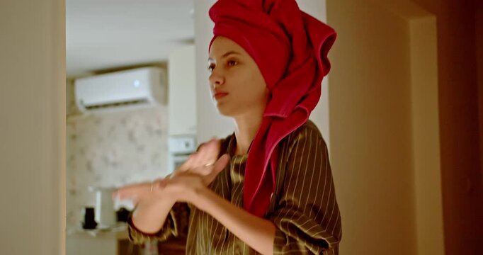 A young woman applies moisturizer to her face in her bathroom as part of her daily beauty routine. She is preparing for the day ahead.