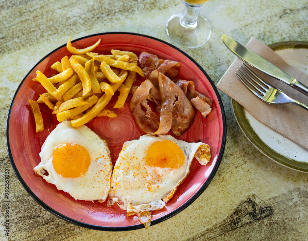 Wall mural hearty and simple homemade breakfast is fried sunny-side up eggs with slices of bacon and side dish 