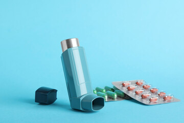 Inhaler and pills on light blue background, closeup. Asthma treatment