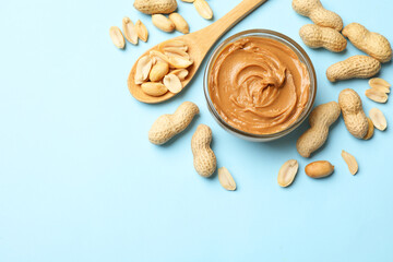 Tasty peanut butter and groundnuts on light blue background, flat lay. Space for text