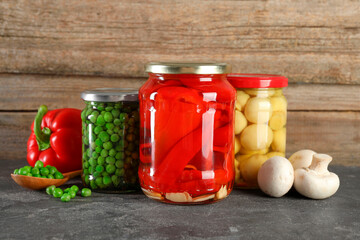 Different pickled products in jars on grey textured table