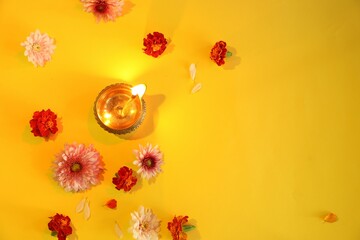 Diwali celebration. Diya lamp and beautiful flowers on yellow background, flat lay. Space for text