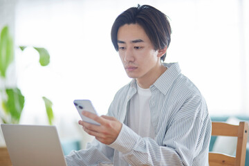 リビングでスマートフォンを使用する日本人大学生の男性