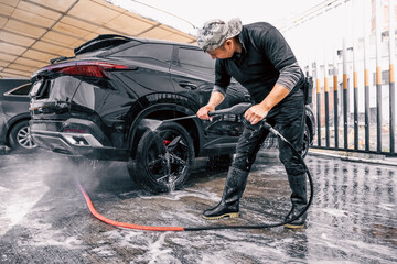 latin man washing a black car with a water pressure machine at a carwash