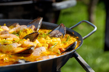 Close up while cooking a paella with vegetables, pork and seafood outdoors