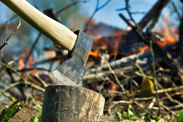 Axe stuck in a log against burning campfire