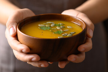 Pumpkin soup in wooden bowl holding by hand, Homemade food in autumn season