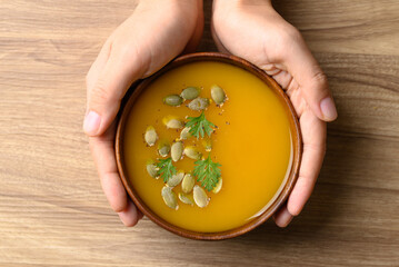 Pumpkin soup in wooden bowl with hand on wooden background, Homemade food in autumn season, Table...