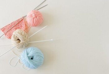 Knitting cloth and knitting needles pastel colors on light beige background top view with copy space. Handmade hobbie concept. 