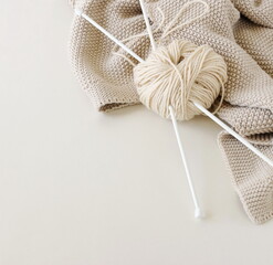 Knitting cloth and knitting needles beige color on light beige background top view with copy space....