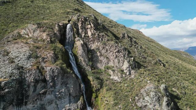 Aerial orbits Caryacuyo waterfall on steep, arid mountainside in Peru